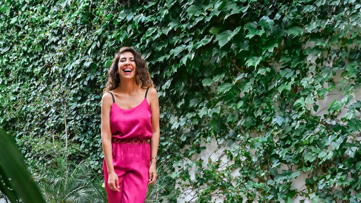 Gaby Caresani riéndose frente a un muro de hiedra, con un enterito rosa