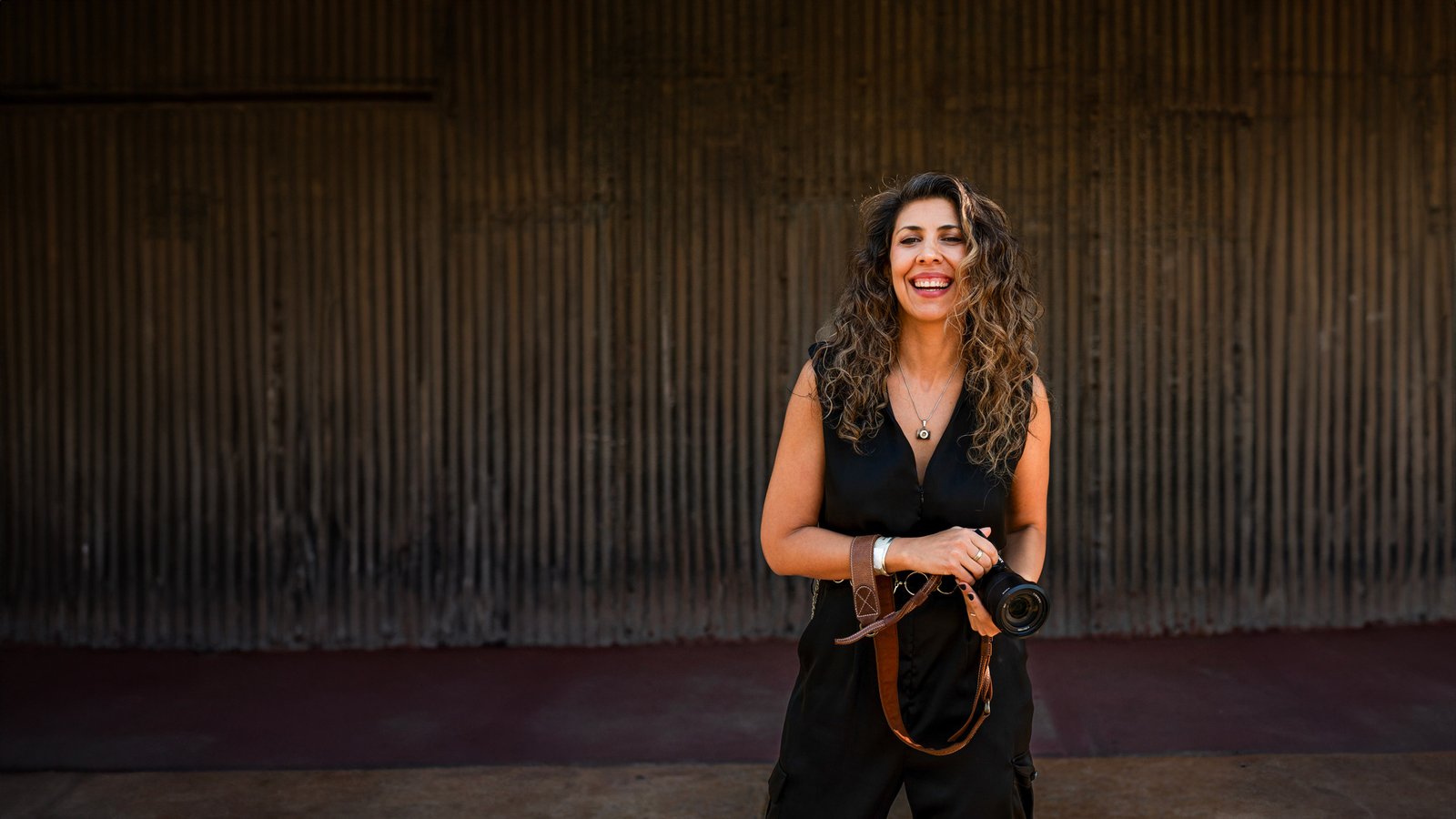 Gaby Caresani sonriendo, con su cámara en las manos, frente a un muro oscuro