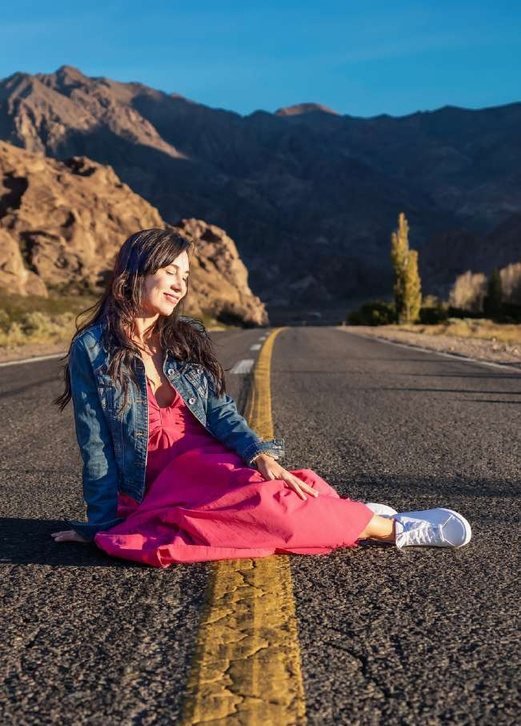 Clienta sentada sobre una ruta con vestido rosa y campera de jean