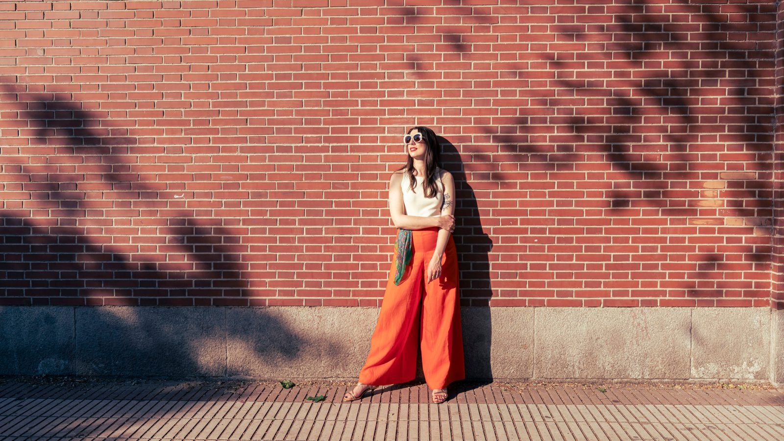 Clienta con pantalón naranja apoyada en una pared de ladrillo en Madrid