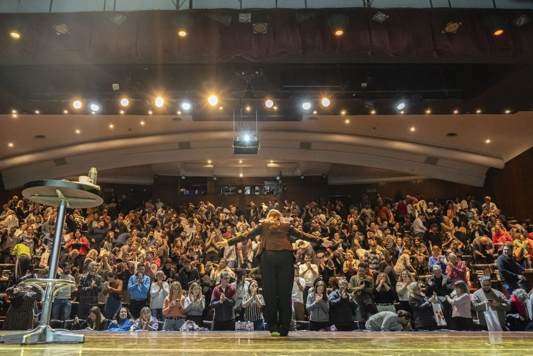 Oradora con los brazos abiertos frente al público en un auditorio