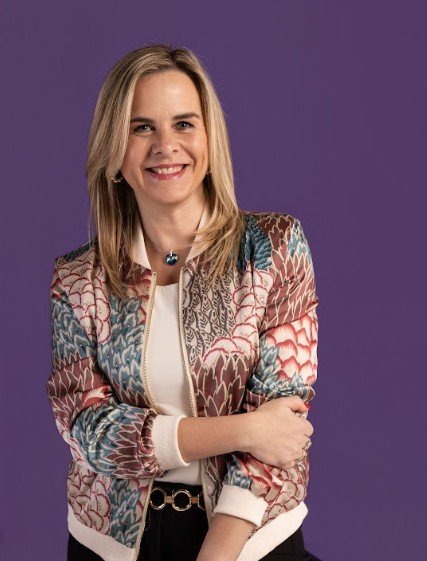 Gisella Dobal sonriendo, con campera estampada sobre fondo violeta